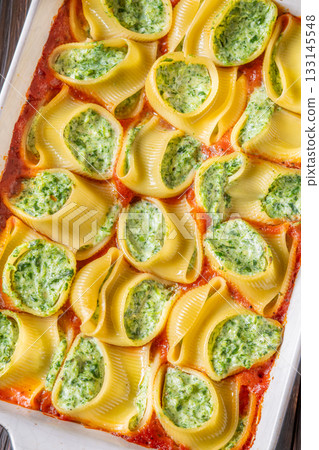 Golden baked lumaconi filled with ricotta and spinach resting in rich tomato sauce 133145548