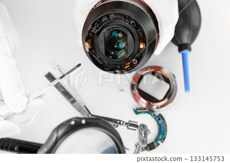 the hands of the master with gloves and a broken lens of a professional camera. 133145753