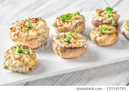Melted blue cheese fills baked mushroom caps creating savory aroma on simple white plate 133145785
