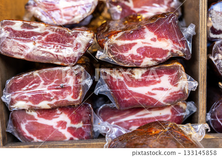 Vacuum-sealed cured meat pieces form layered stacks with rich marbling and deep color. market display shows texture, freshness and artisanal quality of traditional delicacy 133145858