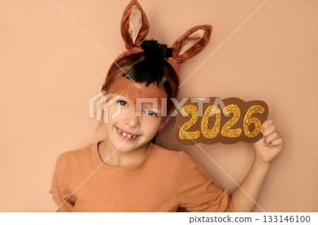 A cute sweet child in a fire horse costume with a painted face, with ear-shaped headbands, shows big numbers 2026. The symbol of the new year A cute sweet child in a fire horse costume with a painted face, with ear-shaped headbands, shows big numbers 2026. The symbol of the new year 133146100