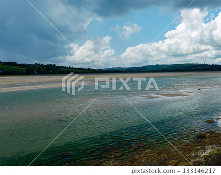 Breathtaking view of water meeting land, from the vibrant green water to the soft sand, leading to rolling hills. The sky is dotted with clouds, enhancing the image. Breathtaking view of water meeting land, from the vibrant green water to the soft sand, leading to rolling hills. The sky is dotted with clouds, enhancing the image. 133146217