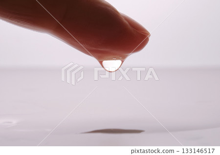 Finger dripping water forming a perfect drop 133146517
