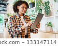 A Woman Happily Using a Tablet Surrounded by Indoor Plants in a Bright and Welcoming Space 133147114