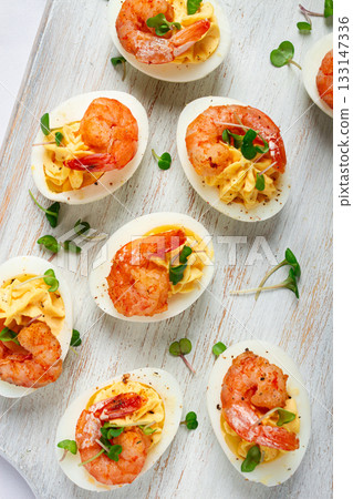 Boiled eggs stuffed with yolk and seasoned with mayonnaise, stuffed eggs with shrimp, on a white wooden chopping board, selective focus, close-up, without people, Boiled eggs stuffed with yolk and seasoned with mayonnaise, stuffed eggs with shrimp, on a white wooden chopping board, selective focus, close-up, without people, 133147336