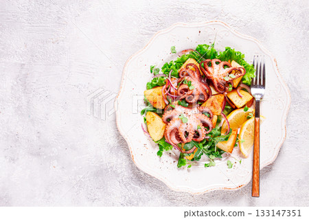 Grilled octopus with baked potatoes and fresh herbs, on a decorative light plate, homemade, no people Grilled octopus with baked potatoes and fresh herbs, on a decorative light plate, homemade, no people 133147351