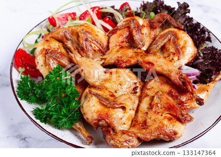 Baked quail, served on a plate with crispy lettuce leaves, fresh tomatoes and herbs, on a white plate, homemade, 133147364