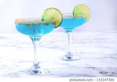 Colorful blue cocktails in elegant glasses with lime garnish on a marble table Colorful blue cocktails in elegant glasses with lime garnish on a marble table 133147380