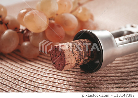 A corkscrew with a wine bottle stopper, lying on a woven napkin, with green grapes, A corkscrew with a wine bottle stopper, lying on a woven napkin, with green grapes, 133147392