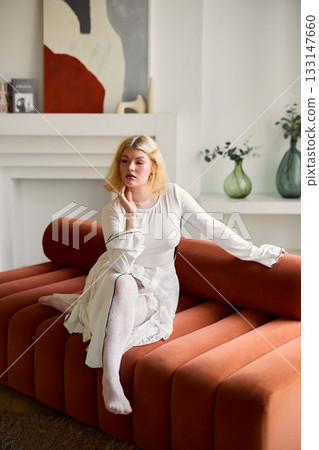 Chic female model seated on vibrant sofa in cozy setting 133147660