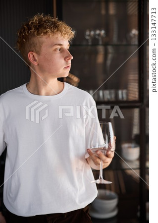 Informal portrait of blond man holding glass in sleek kitchen 133147713