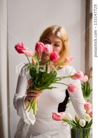 Woman in white adjusts vibrant tulips on her domestic kitchen Woman in white adjusts vibrant tulips on her domestic kitchen 133147729