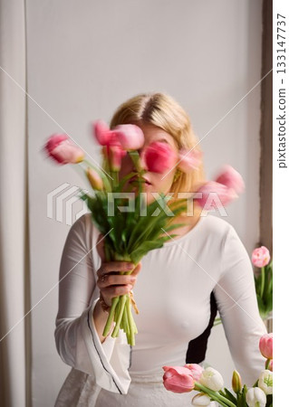 Caucasian blonde posing amid blurred tulips in artistic setting 133147737