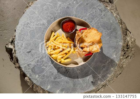 Enjoy Classic Fish and Chips with Ketchup on a Stylish Stone Surface for enhanced flavor 133147755