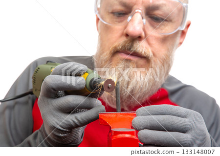 A skilled craftsman in safety goggles focuses intently on a rotary tool as he grinds A skilled craftsman in safety goggles focuses intently on a rotary tool as he grinds 133148007