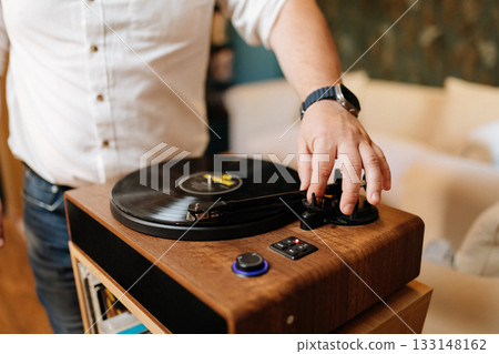 Hand lowering tonearm on vinyl record player, cozy home audio setup 133148162