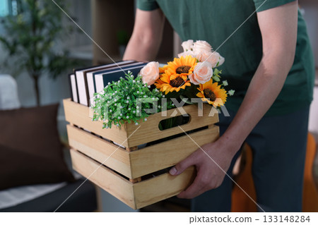 Close-up of hands carrying a crate with flowers and books Close-up of hands carrying a crate with flowers and books 133148284