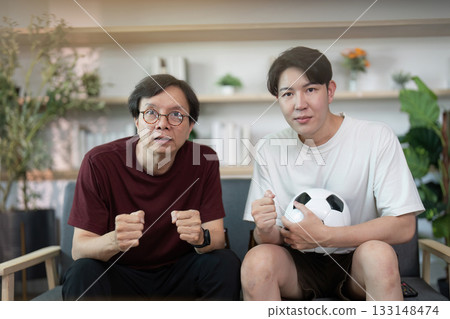 Excited father and son cheering for soccer team at home Excited father and son cheering for soccer team at home 133148474
