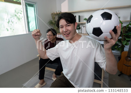 Excited son celebrating soccer victory with father in living room Excited son celebrating soccer victory with father in living room 133148533