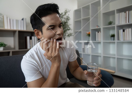 Dental Discomfort. Man holding jaw in pain while sitting with water. 133148584