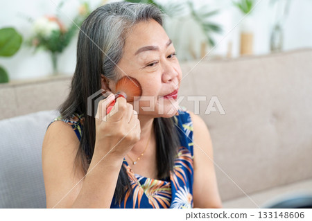 Makeup Application. Mature woman applying blush with a brush in front of a mirror. 133148606