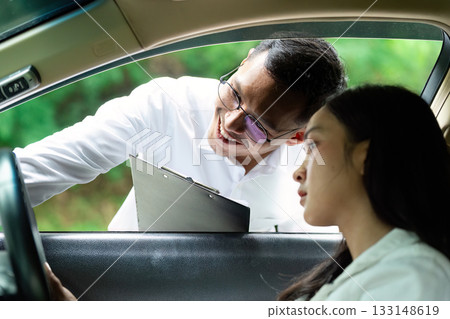 Insurance Consultation. A man smiling while discussing car insurance with a woman in a vehicle. 133148619