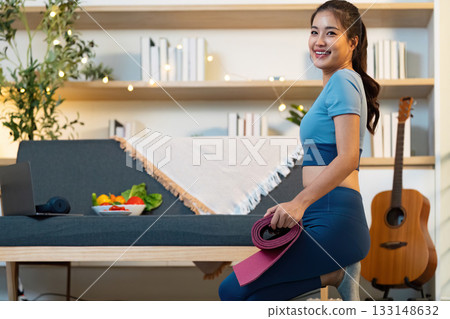 Yoga and Fitness. Smiling woman with yoga mat in cozy home setting. Yoga and Fitness. Smiling woman with yoga mat in cozy home setting. 133148632