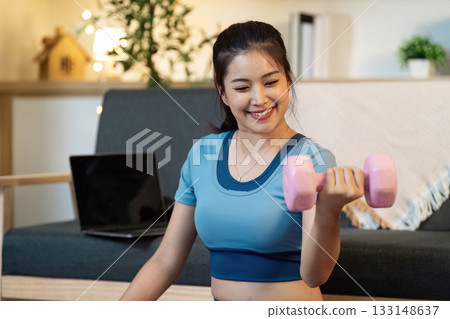 Fitness Motivation. Woman lifting pink dumbbell while smiling at home. Fitness Motivation. Woman lifting pink dumbbell while smiling at home. 133148637