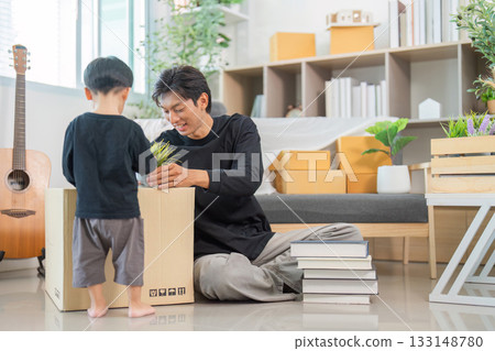 Father and son unpacking and arranging items in a bright living room 133148780