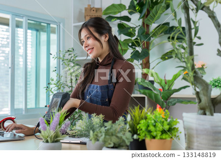 Sustainable Gardening. Smiling woman in apron engaging with customers in a plant shop. 133148819