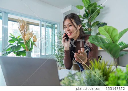 Remote Work. Woman on phone discussing plant care in a home office. 133148852