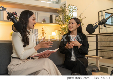 Podcast Interview. Two women discussing ideas while seated on a cozy couch. 133148994