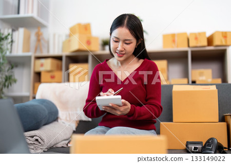 E-commerce businesswoman taking notes while organizing packages 133149022