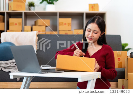 E-commerce. Woman managing inventory and packaging orders at home office. 133149033