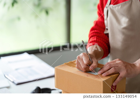 E-commerce Operations. A person labeling packages while managing logistics in a modern workspace. 133149054