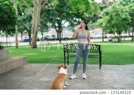 Wellness and Hydration. Woman refreshing herself and her corgi in a park. Wellness and Hydration. Woman refreshing herself and her corgi in a park. 133149128