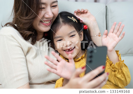 Mother and Daughter Video Call. Joyful moments shared while waving at family. Mother and Daughter Video Call. Joyful moments shared while waving at family. 133149168