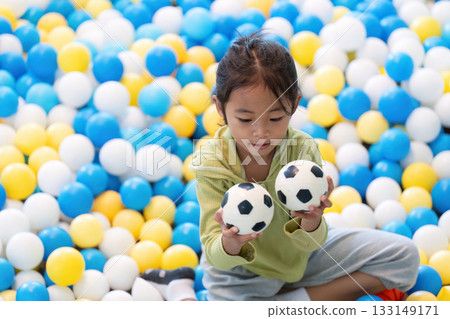 Playful Exploration. A young girl enjoying soccer balls in a colorful ball pit. Playful Exploration. A young girl enjoying soccer balls in a colorful ball pit. 133149171