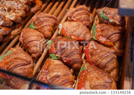 Display of savory croissant sandwiches filled with salmon, cheese and greens on a bakery shelf. Ideal for cafe menus, deli promotions and breakfast marketing Display of savory croissant sandwiches filled with salmon, cheese and greens on a bakery shelf. Ideal for cafe menus, deli promotions and breakfast marketing 133149256