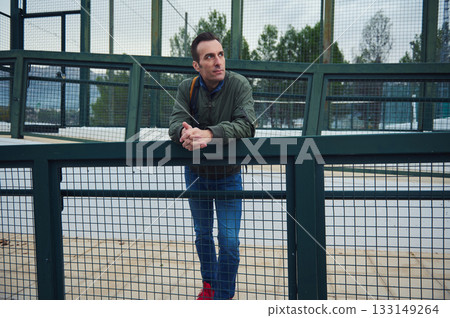 Thoughtful Man Leaning Over Green Fence At Outdoor Park, Casual Moment 133149264