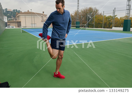Athlete Stretching Leg On Tennis Court During Outdoor Training Session In Casual Gear 133149275