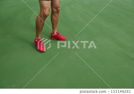 Athlete in Red Shoes Stands on Green Tennis Court Surface During Training Athlete in Red Shoes Stands on Green Tennis Court Surface During Training 133149281