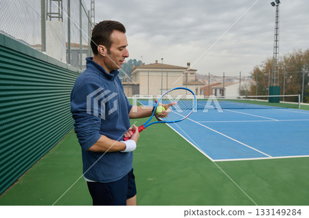 Focused Man Preparing Tennis Serve On Outdoor Blue Court With Racket And Ball 133149284