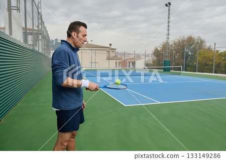 Focused Tennis Player Practicing on Outdoor Court with Racket and Ball 133149286