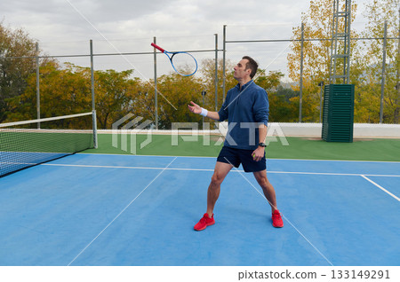 Athletic Man On Tennis Court Tossing Racket In Outdoor Match On Blue Surface 133149291