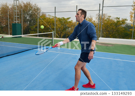 Focused Male Tennis Player in Blue Returns Serve on Outdoor Court With Determination 133149293