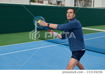 Focused Tennis Player In Blue Long-Sleeve Shirt Aiming Serve On Outdoor Court Focused Tennis Player In Blue Long-Sleeve Shirt Aiming Serve On Outdoor Court 133149296