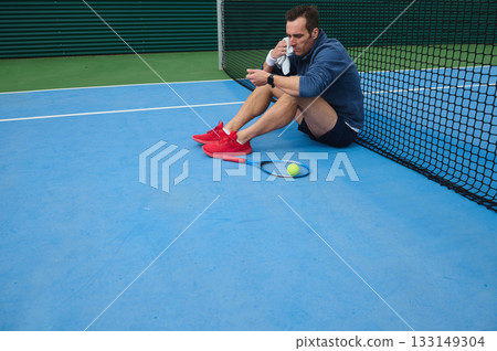 Man Resting After Tennis Practice On Blue Court By Net With Ball And Racket 133149304