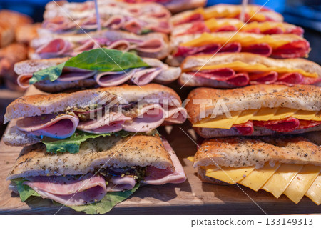 Array of gourmet sandwiches with layered fillings, cheese, ham and greens, displayed ready-to-serve. Commercial food shot suitable for delis, cafes and catering menus 133149313
