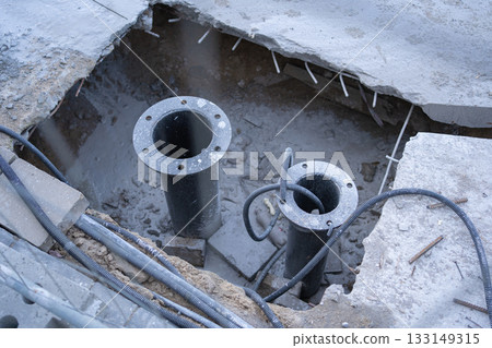Open construction area showing large vertical pipes, cables and concrete debris. A technical scene of urban infrastructure repair and installation work 133149315